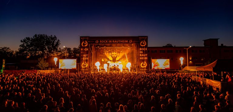 Festivalbühne bei Nacht mit Feuer- und Lichteffekten, großes Publikum vor der Bühne.